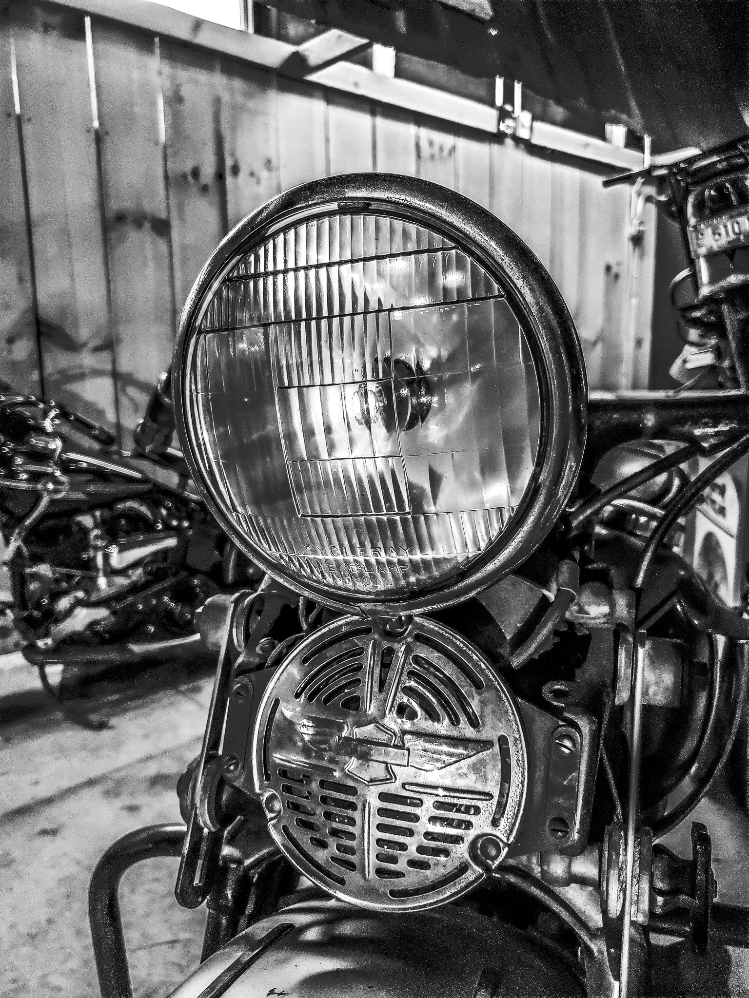Black-and-white close-up of a vintage motorcycle headlight and horn