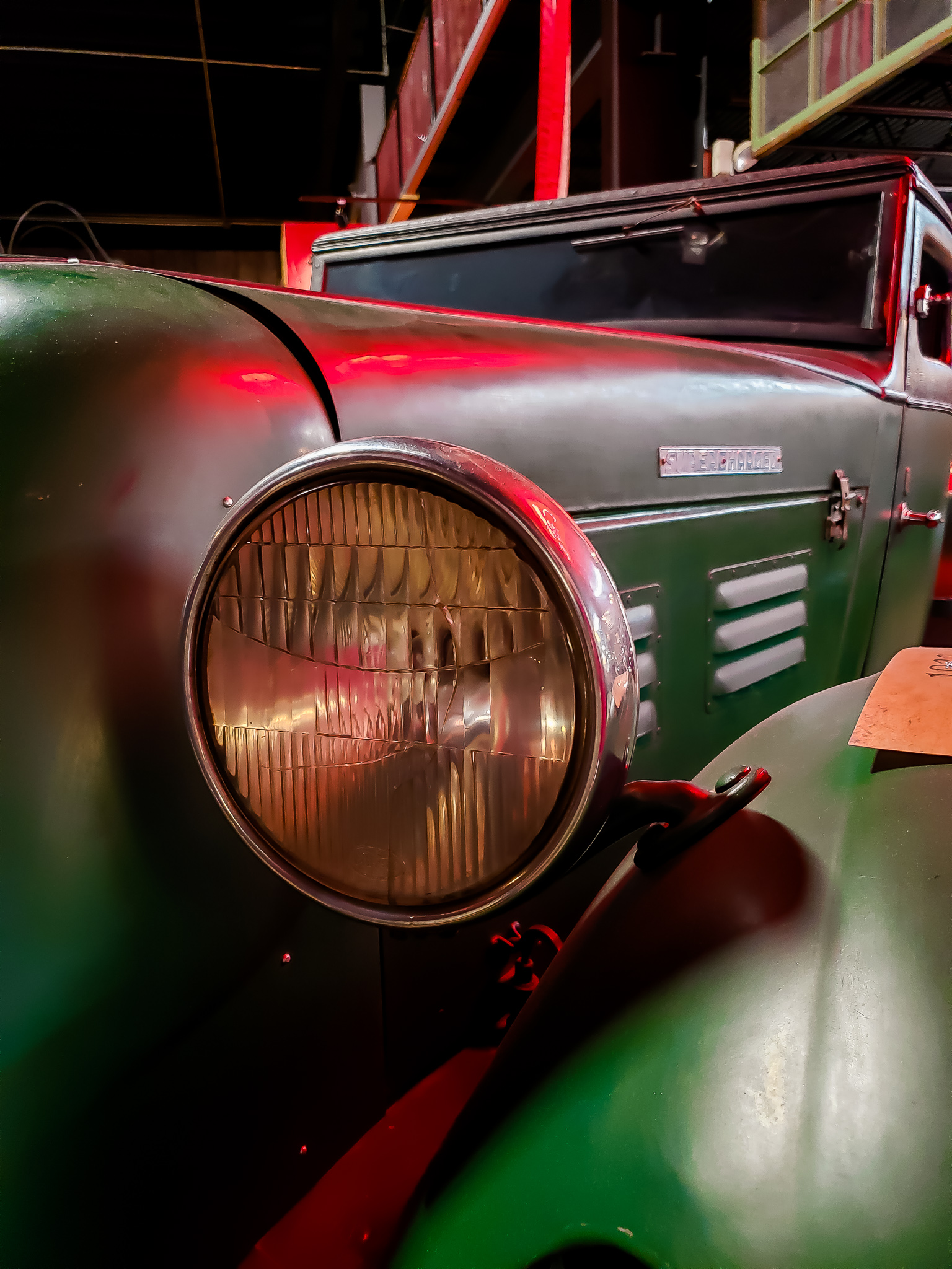 Close-up of a vintage green vehicle headlight reflecting dramatic red light