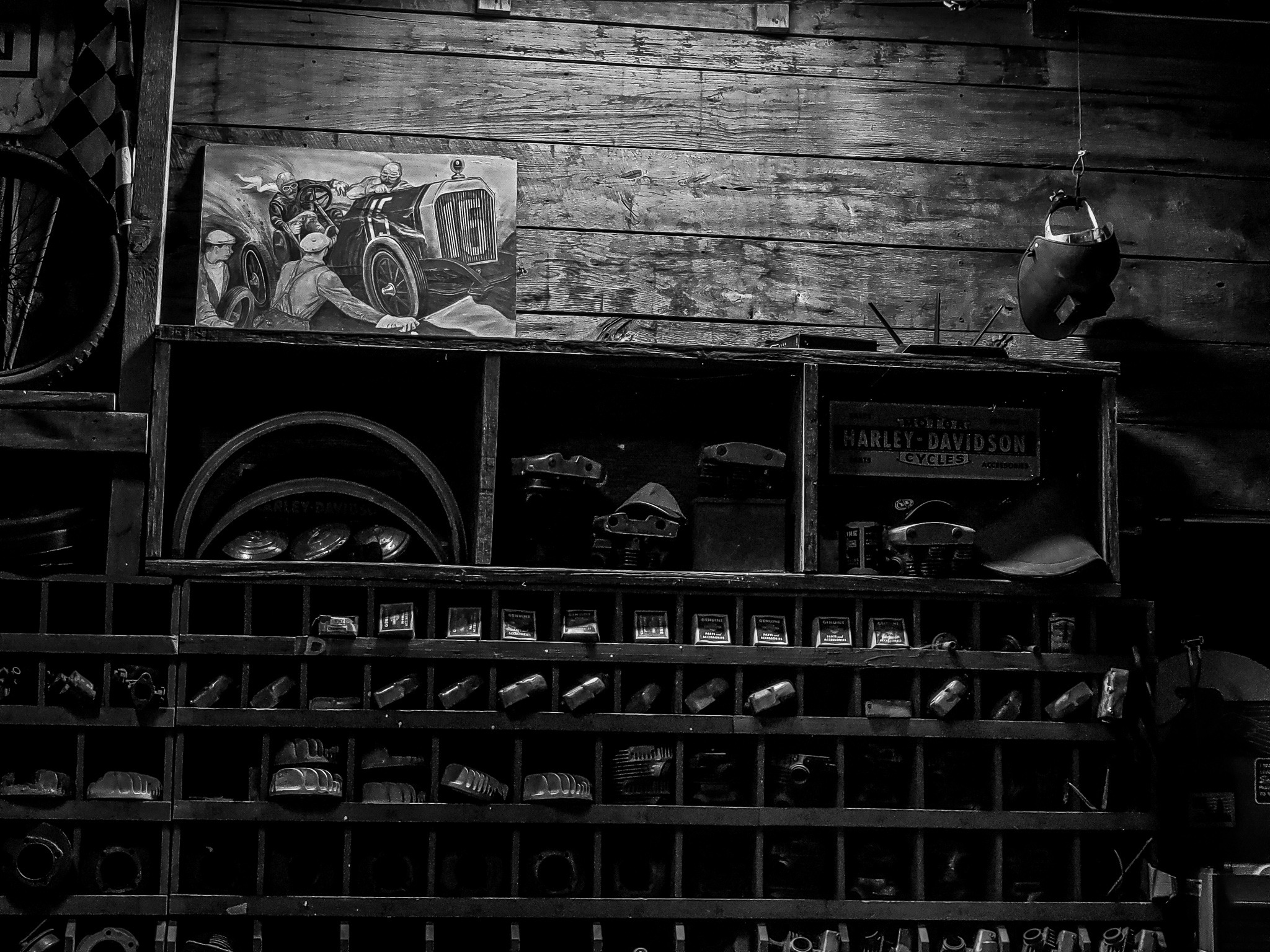 Black-and-white view of a weathered vintage motorcycle workshop wall filled with parts and memorabilia